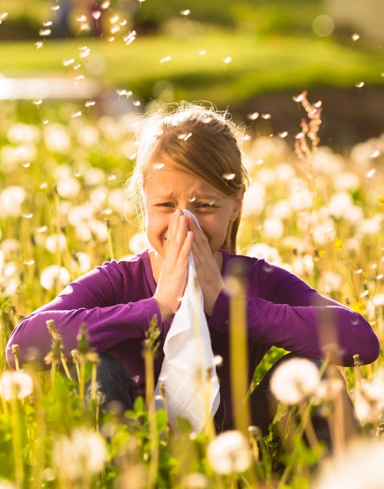girl sitting in meadow with dandelions and has hay fever or allergy