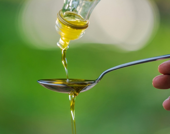 pouring olive oil into spoon on green park garden background